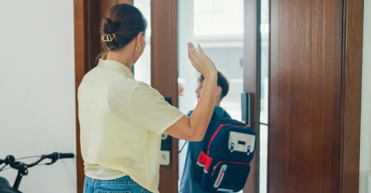 Young mother waves goodbye to her son as he leaves for first day of schooll
