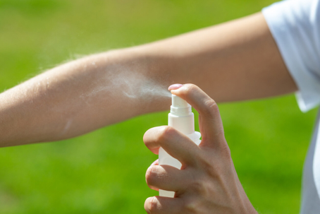 Child spraying bug spray on arm