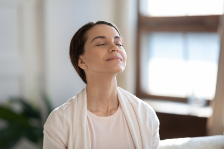 Woman sitting on sofa with closed eyes breathing air.