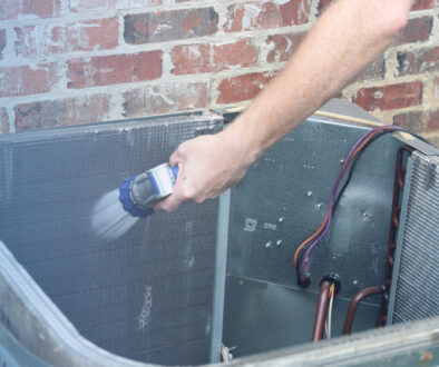 a hand cleaning the inside of a air conditioning unit with a hose