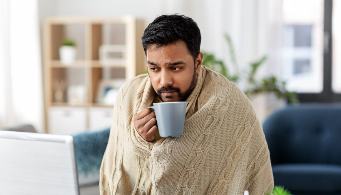 A man wrapped in a warm beige blanket drinking coffee